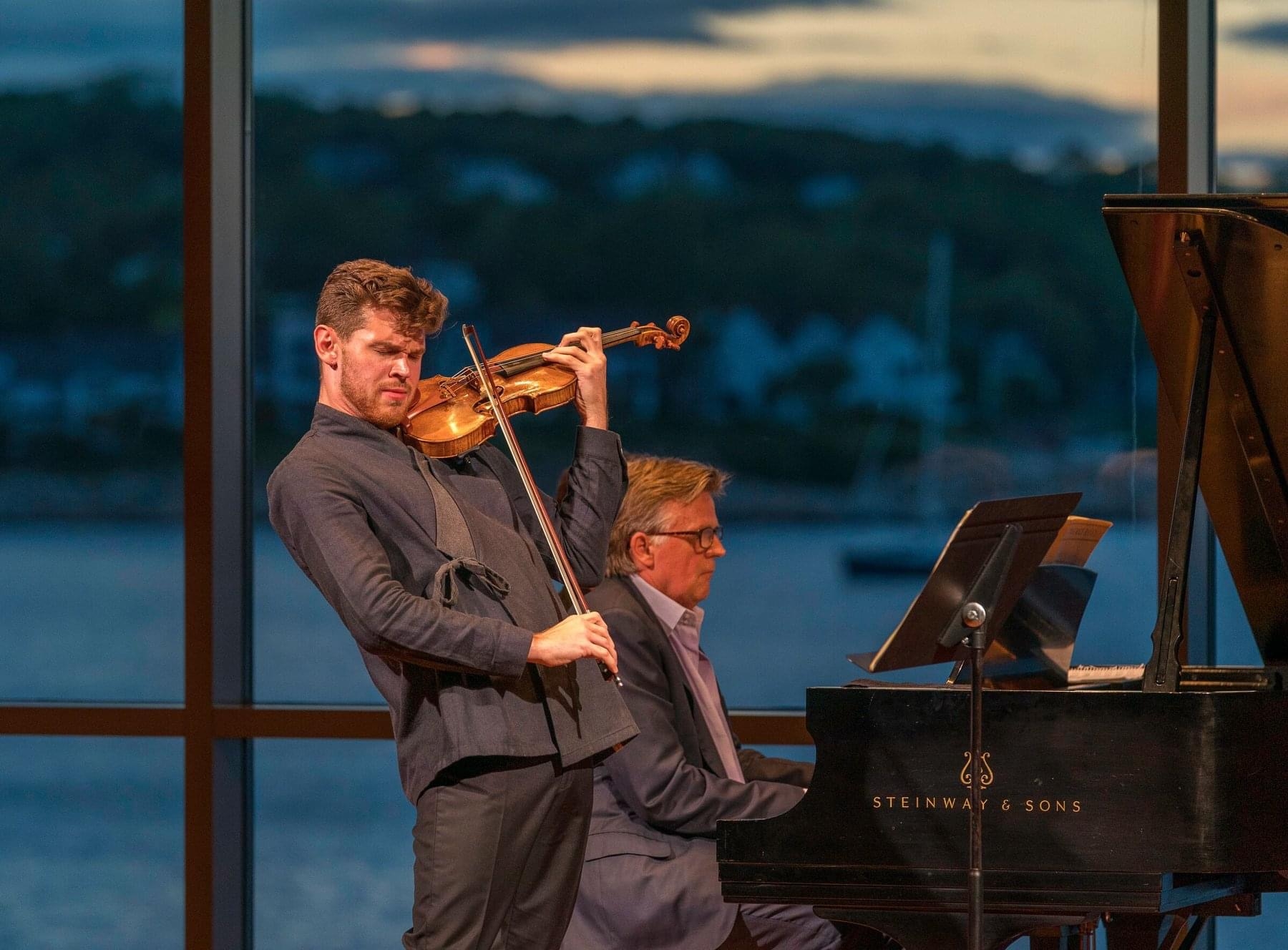Blake Pouliot performing violin with a pianist at sunset